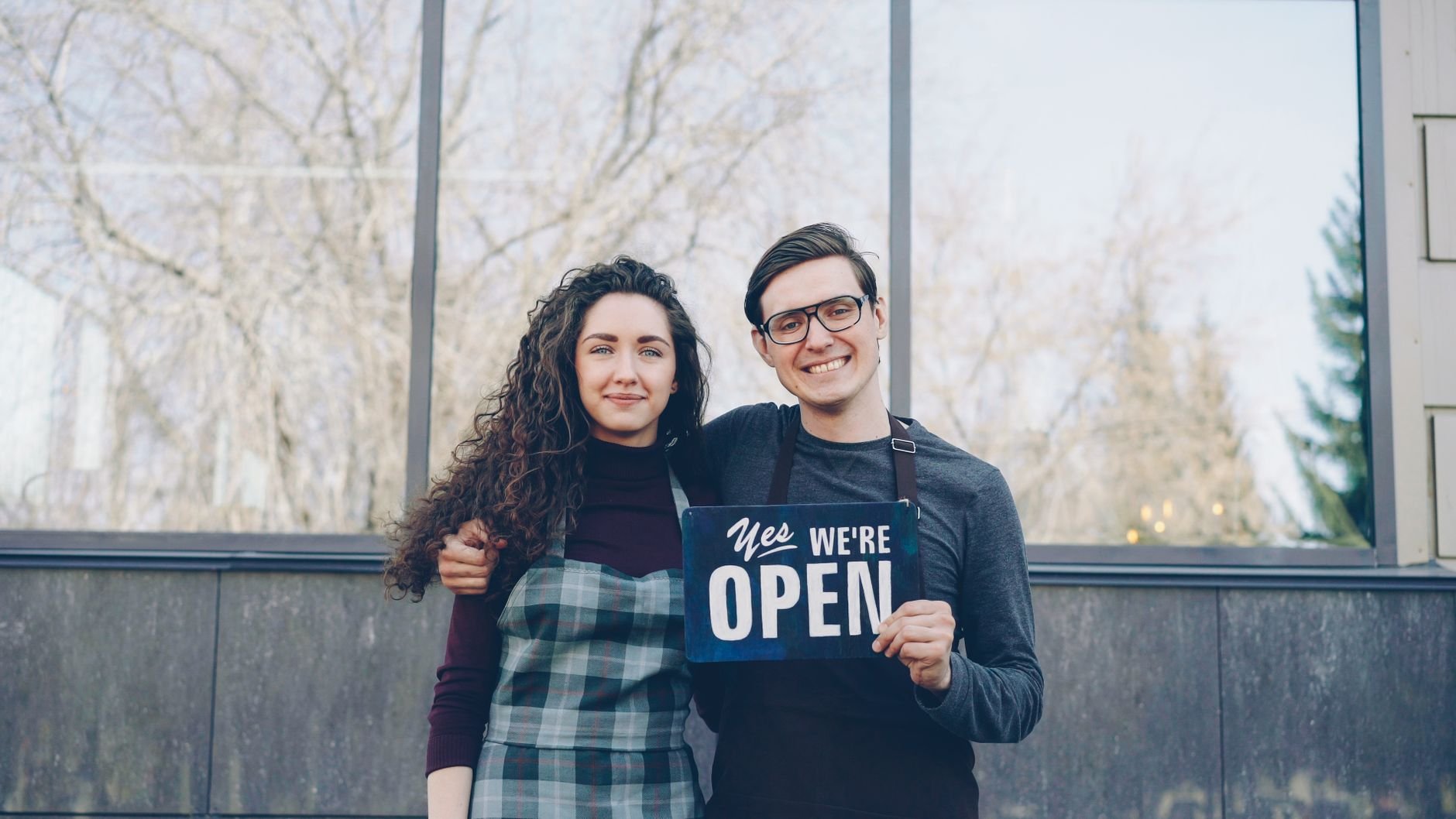 Smiling business owners standing outside their storefront with an open sign